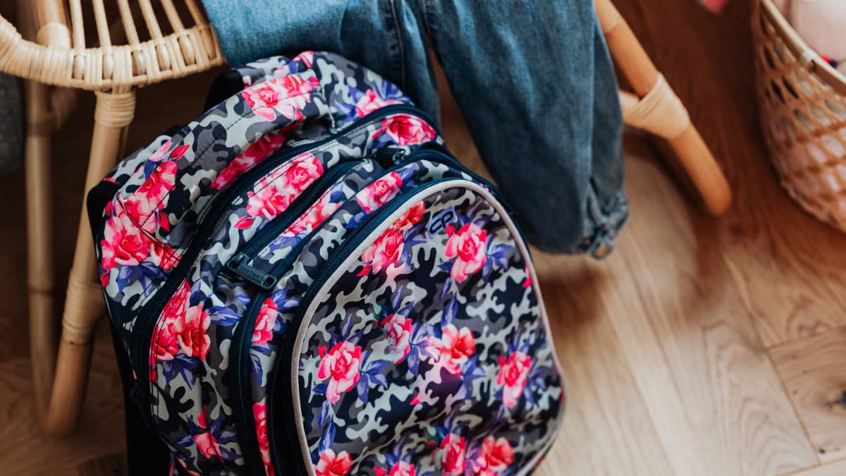 Vibrant floral patterned backpack on a wooden floor beside wooden furniture.